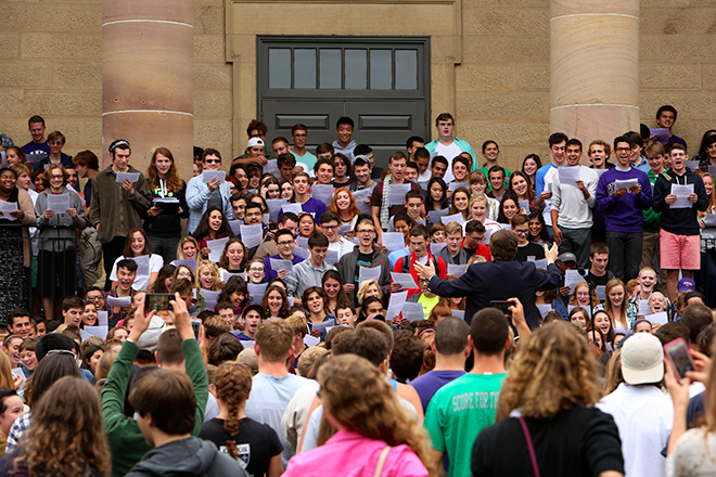 A large group of students sing on the steps of Rosse Hall.