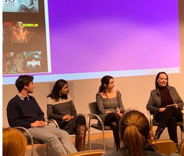 Four members of a panel sit before an audience in front of a large video screen.