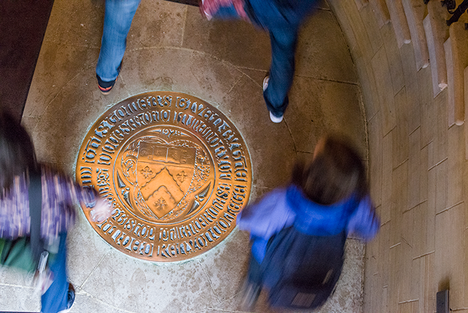 An overhead view of students stepping around a gold seal in Peirce Hall's floor.